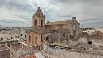 Um edifício histórico com uma torre de sino e uma grande porta em arco, rodeado por construções urbanas.