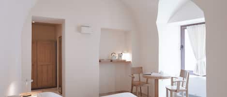 A hotel room with a bed, a desk, two chairs, a small table with a lamp, and a window with curtains.