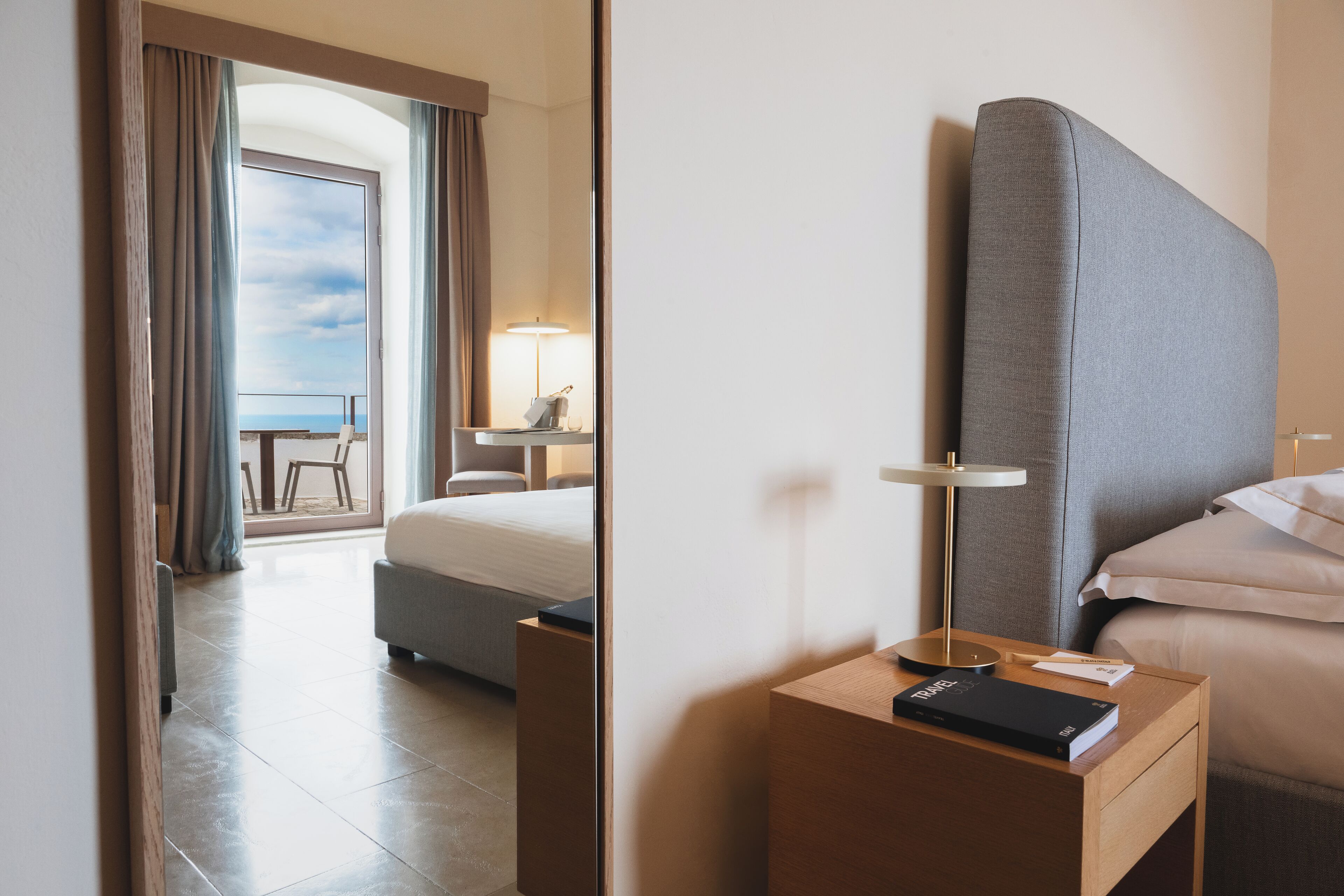 Ein Hotelzimmer mit Bett, Nachttisch, Lampe und Blick auf den Balkon.