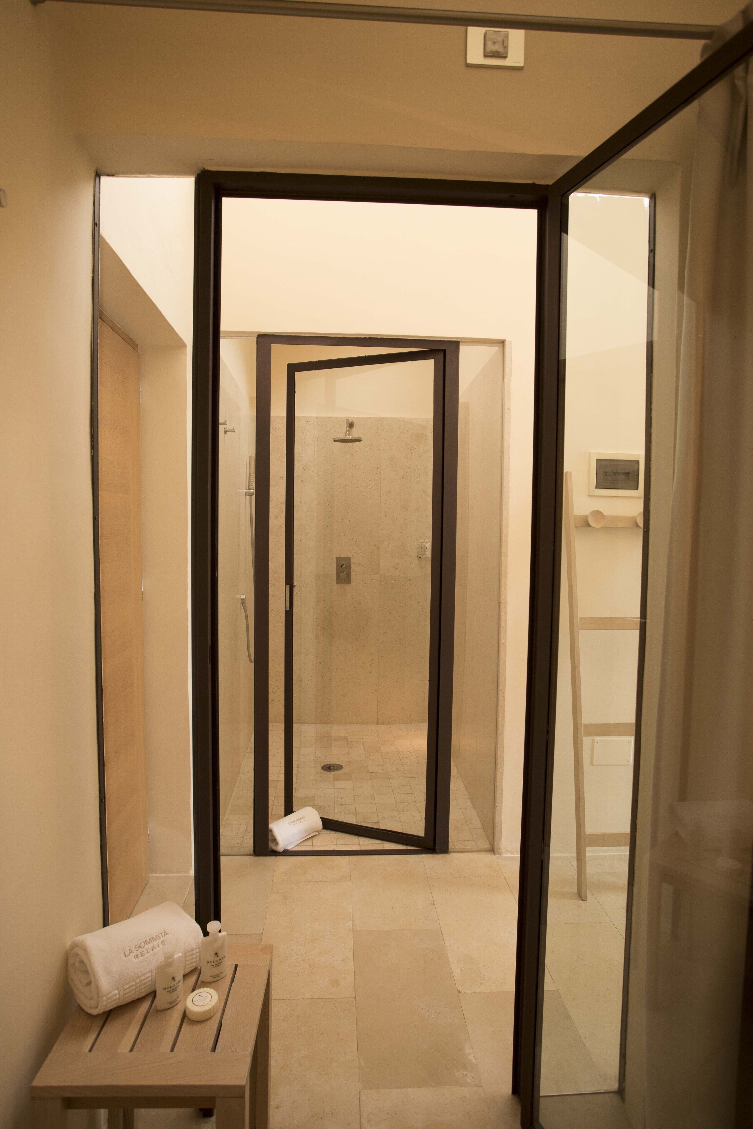 A modern bathroom with a glass shower enclosure, a wooden table with toiletries, and a towel.