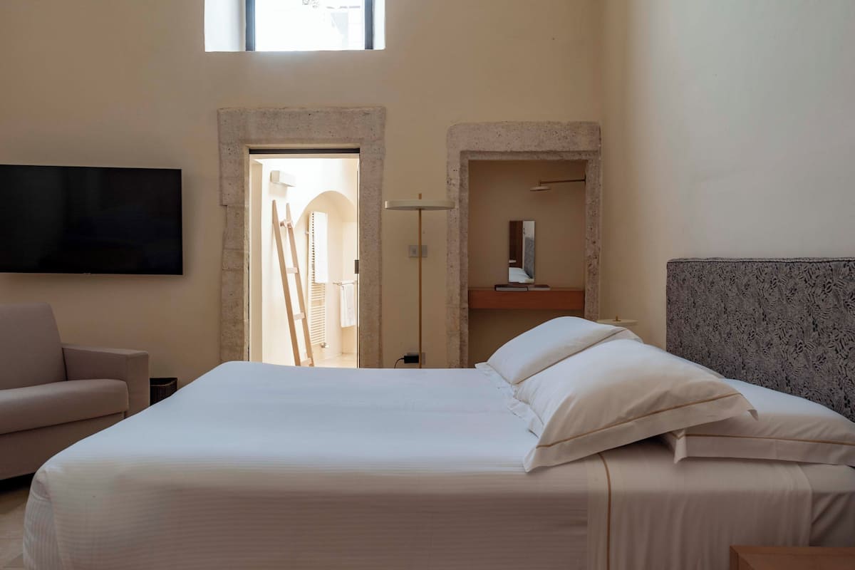 Ein Hotelzimmer mit einem großen Bett, einem flachbildfernseher an der Wand, einem Sofa und einem kleinen Tisch.