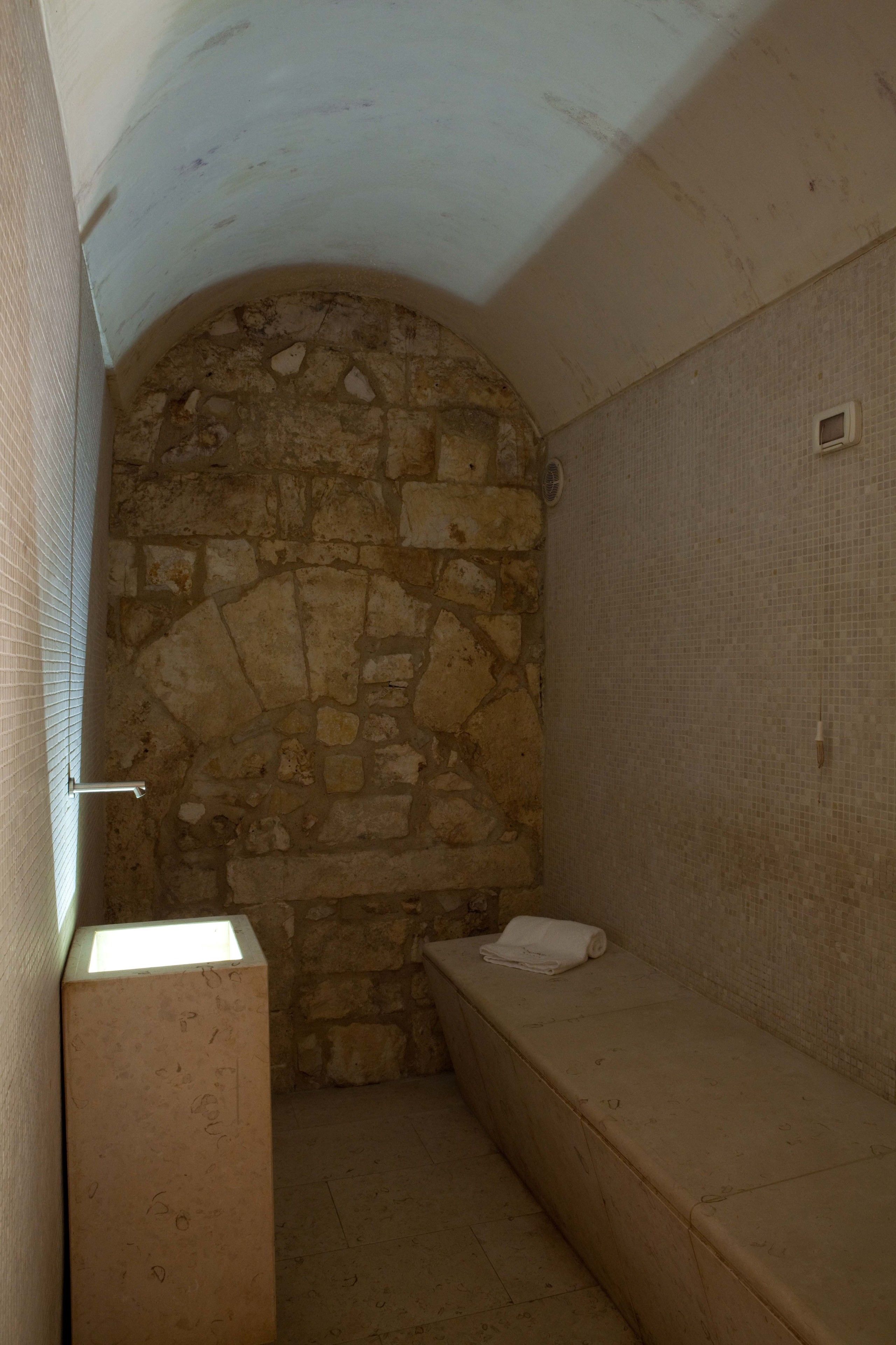 Un baño pequeño con paredes de piedra, un banco y un lavamanos.
