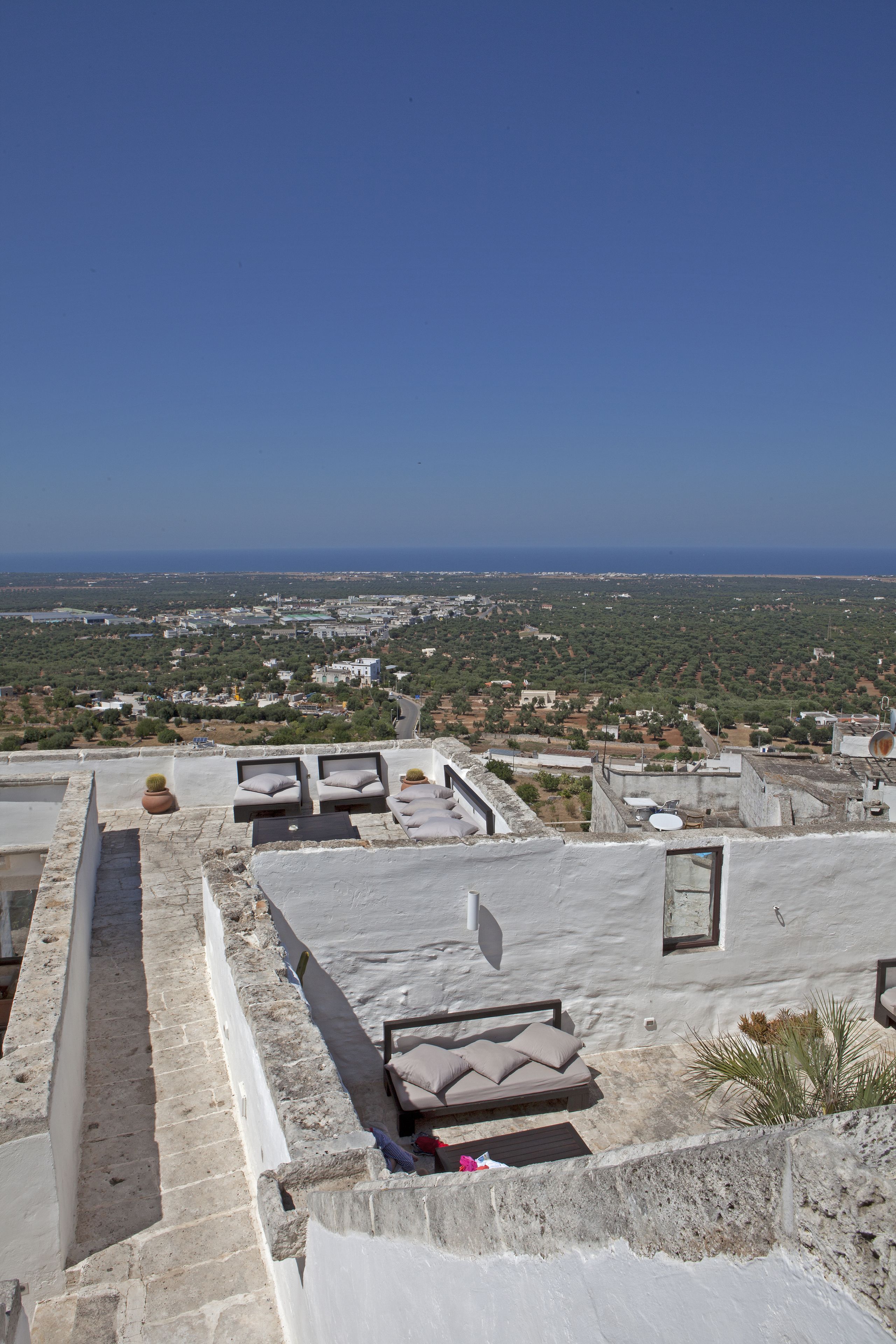 A rooftop terrace with lounge chairs and a view of a coastal town.