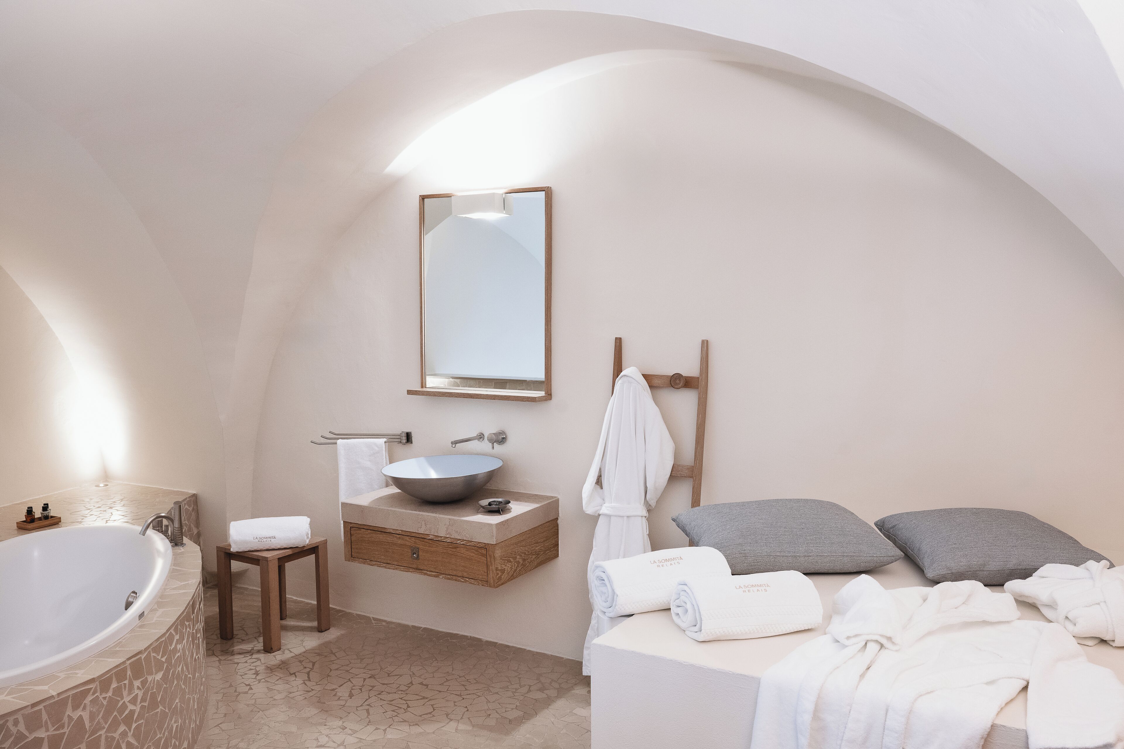 A modern bathroom with a freestanding bathtub, a vanity with a bowl sink, and a bed with pillows.