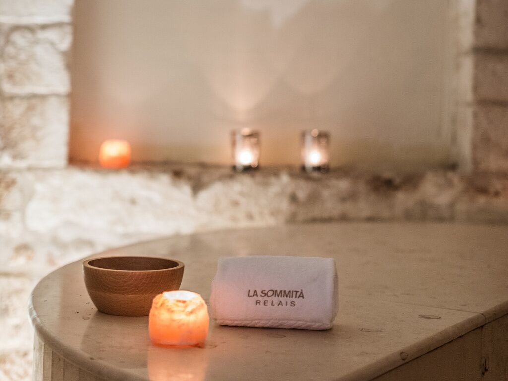 Un muro de piedra con velas y un cuenco de madera sobre una mesa.