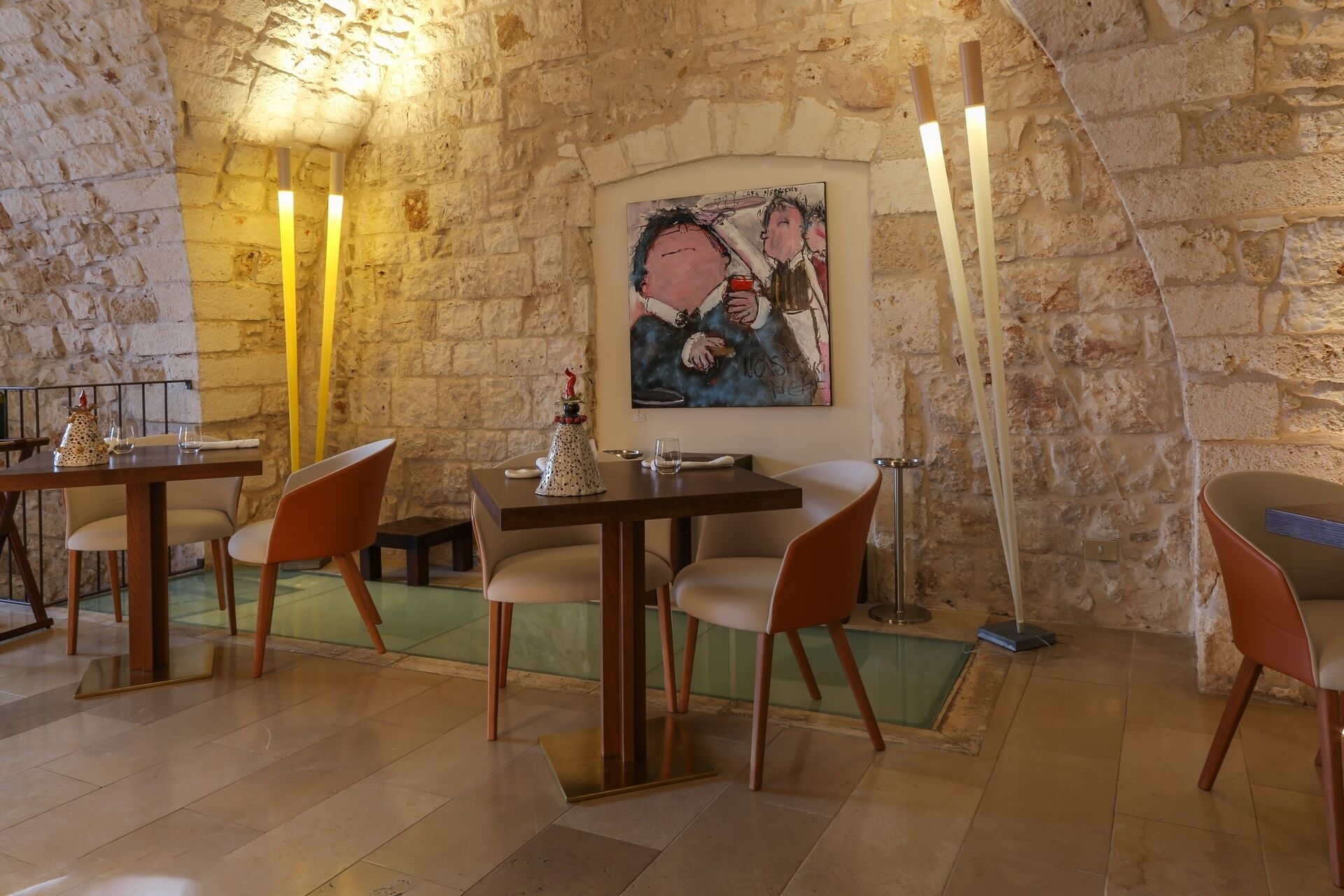 Un restaurante con paredes de piedra, mesas y sillas de madera. Hay un cuadro en la pared y velas en las mesas.