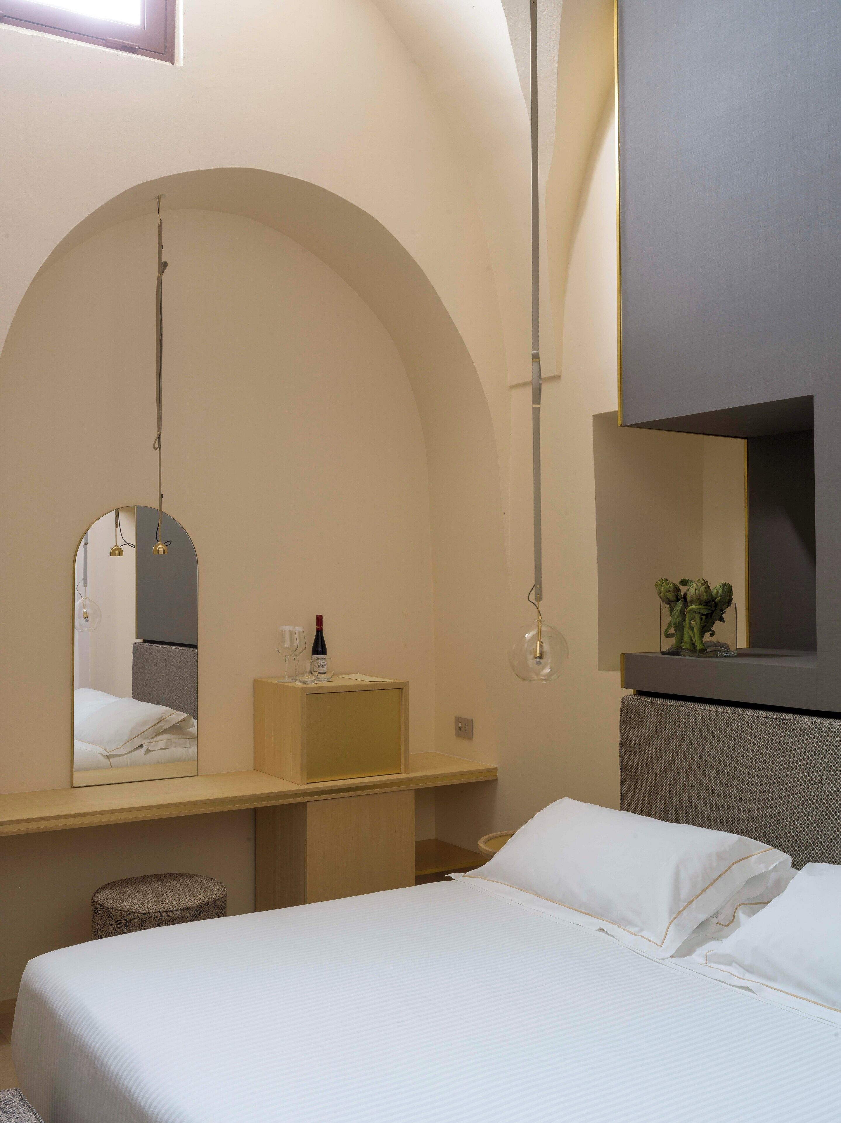 Un dormitorio moderno con una cama, un tocador con espejo, una lámpara colgante y una planta pequeña en la cómoda.