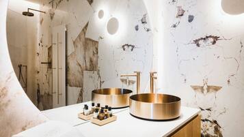 A bathroom with a marble wall, a sink with two basins, and a towel on the counter.