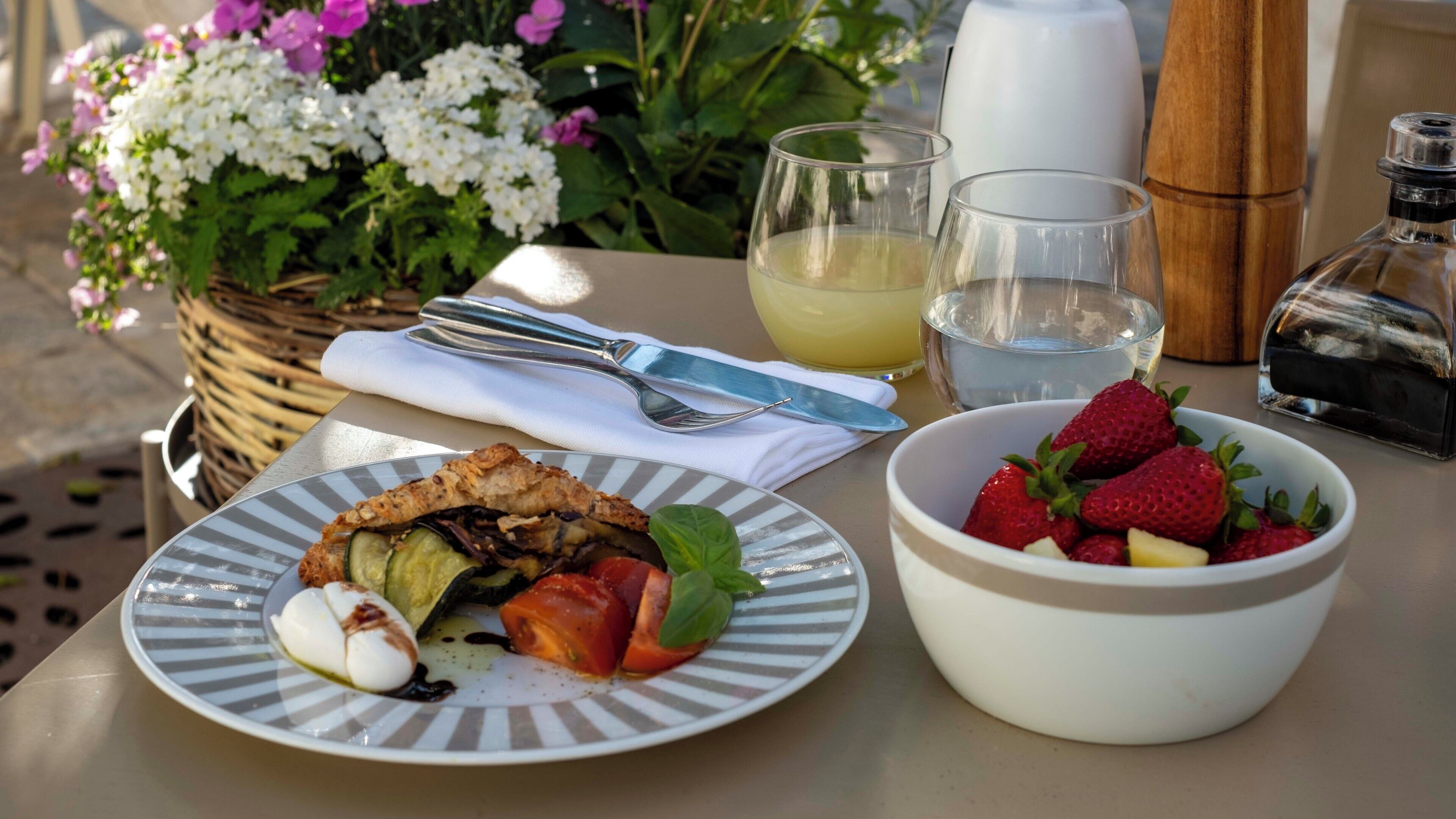 A table with a plate of food, a bowl of strawberries, a glass of water, and a bottle of olive oil.
