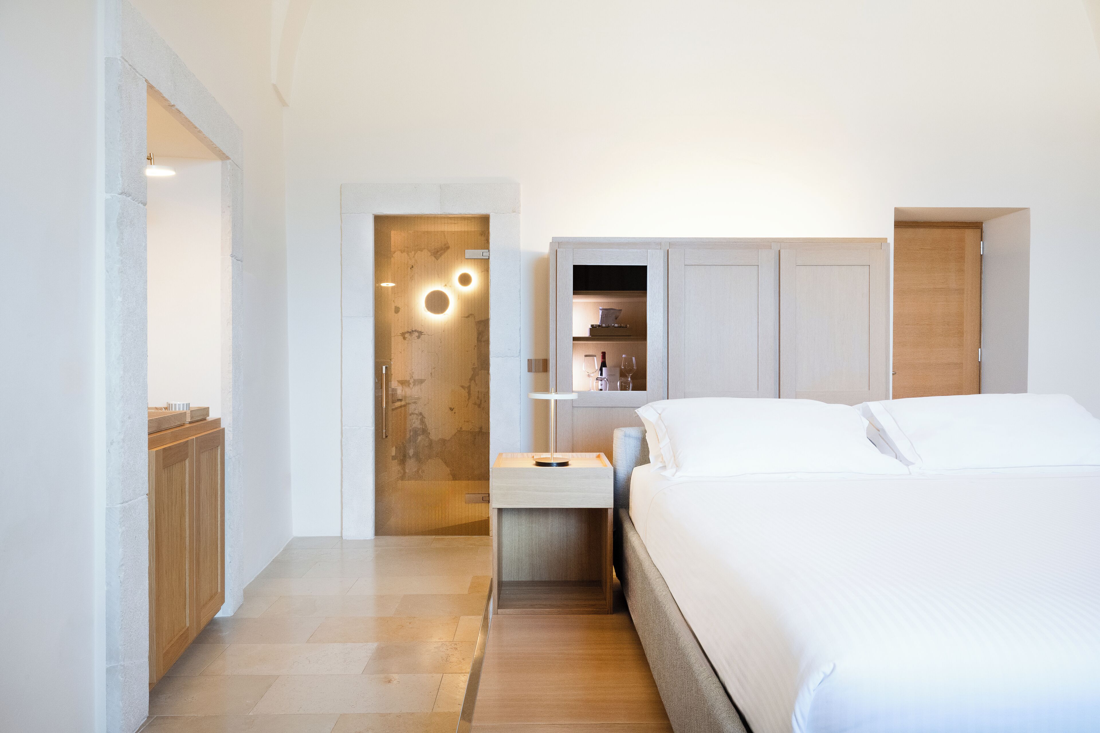 Un dormitorio moderno con una cama grande, una mesita de noche, un armario de madera y un estante empotrado con una lámpara.