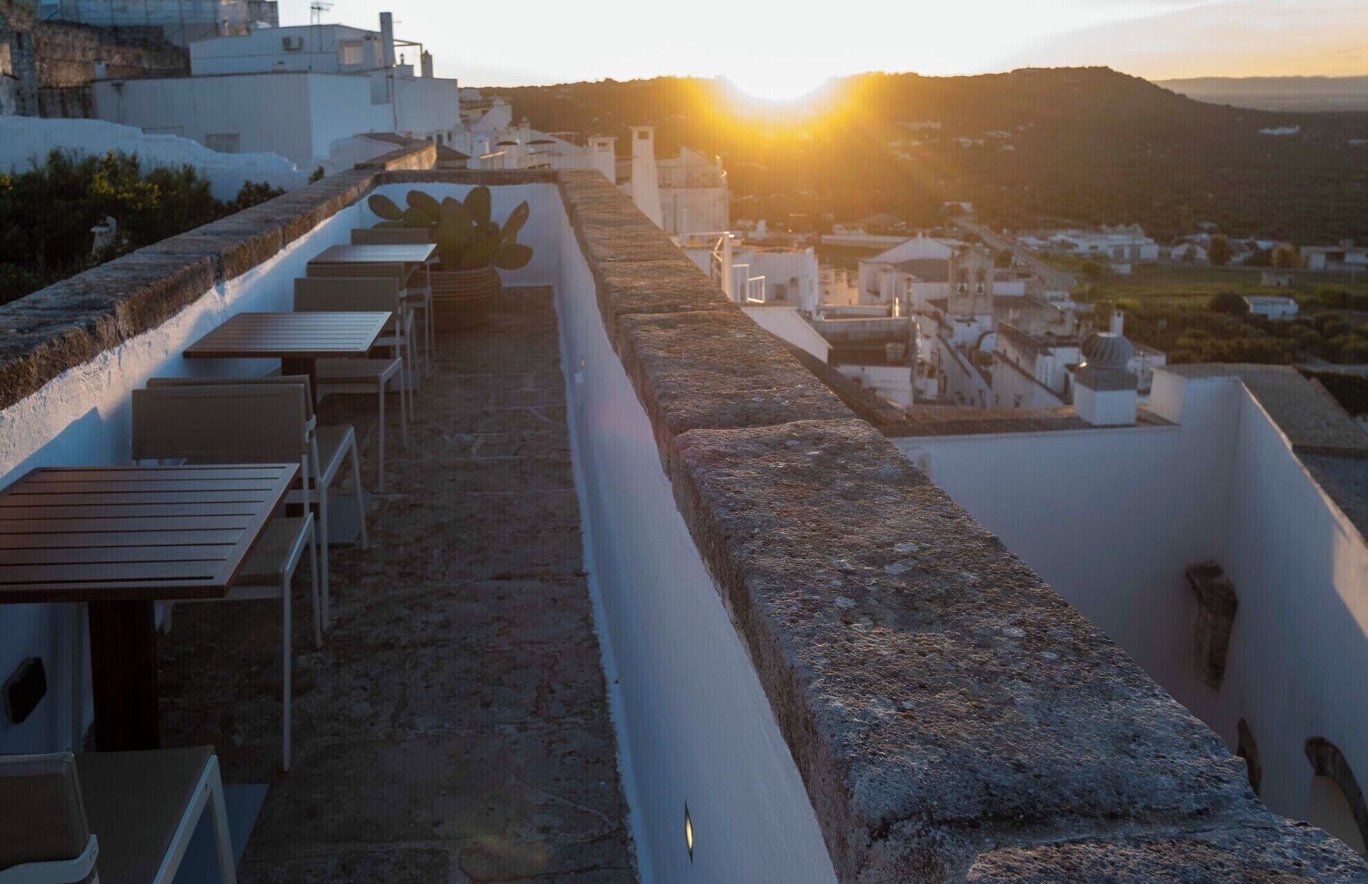 A rooftop terrace with outdoor seating and a view of a hillside town during sunset.