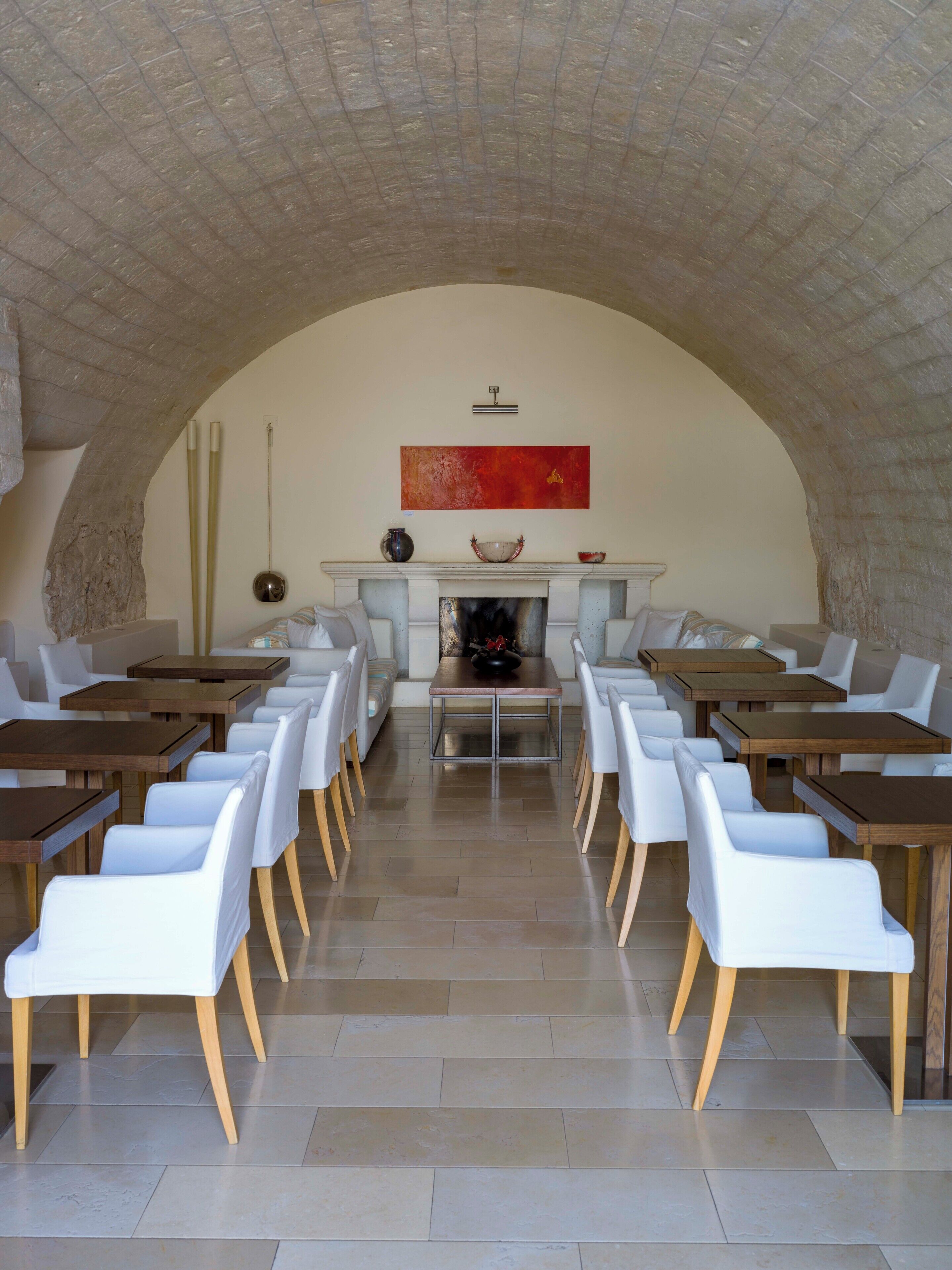Un espace repas avec une cheminée, des chaises blanches et de longues tables.