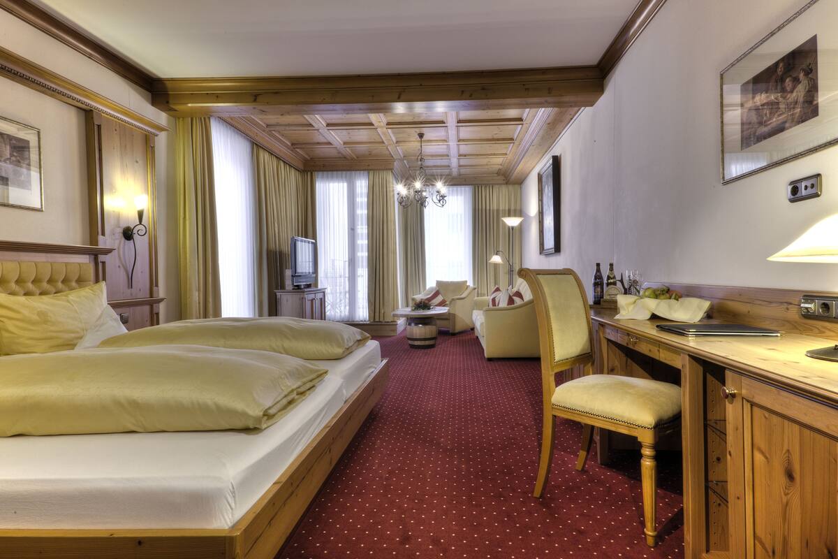 Ein Hotelzimmer mit einem großen Bett, einem Schreibtisch, einem Sessel, einem kleinen Tisch und einem Fernseher.