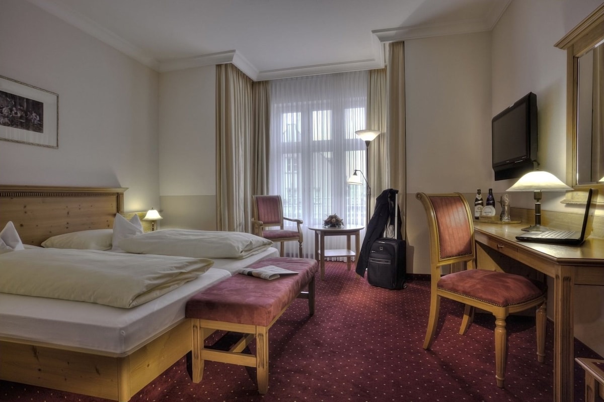A hotel room with two beds, a desk with a laptop, a chair, a small table, and a television.