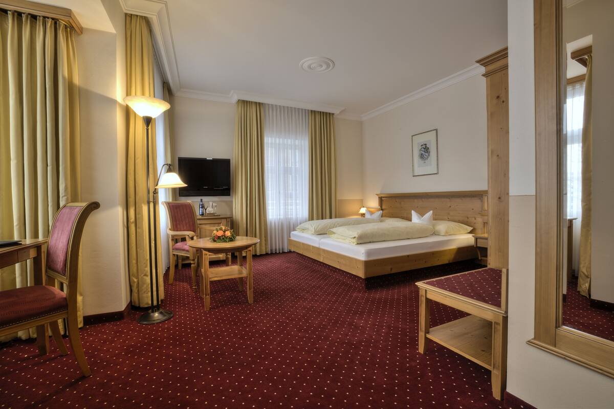 Ein Hotelzimmer mit Bett, Schreibtisch, Stuhl, Lampe und Fernseher.
