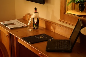 A wooden desk with a laptop, a bottle of champagne, a glass, and a newspaper.