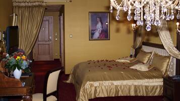 Una camera d'albergo con un grande letto, un lampadario, un quadro appeso e una scrivania con un vaso di fiori.