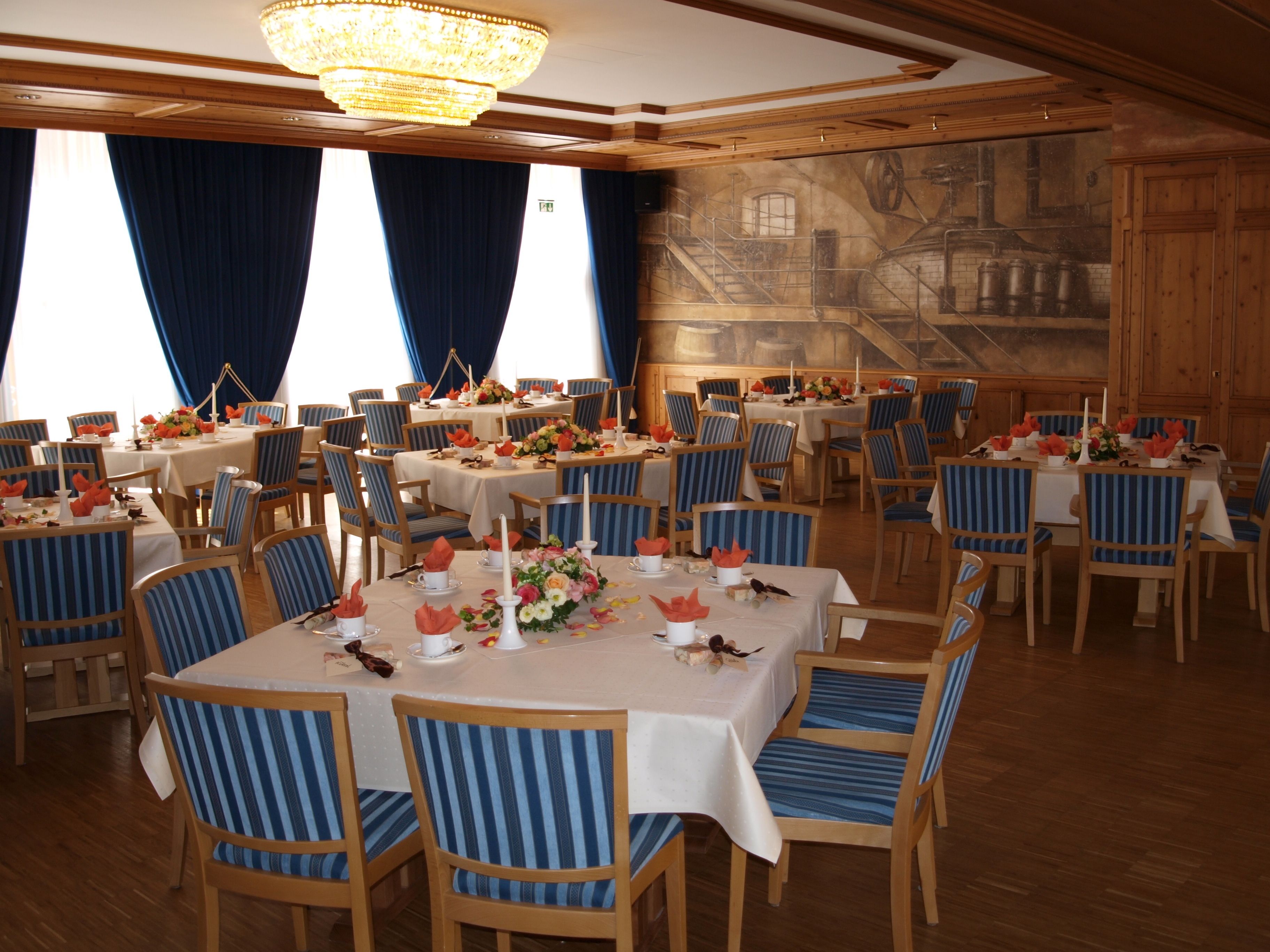 A dining area with multiple tables, blue-striped chairs, white tablecloths, and a chandelier.