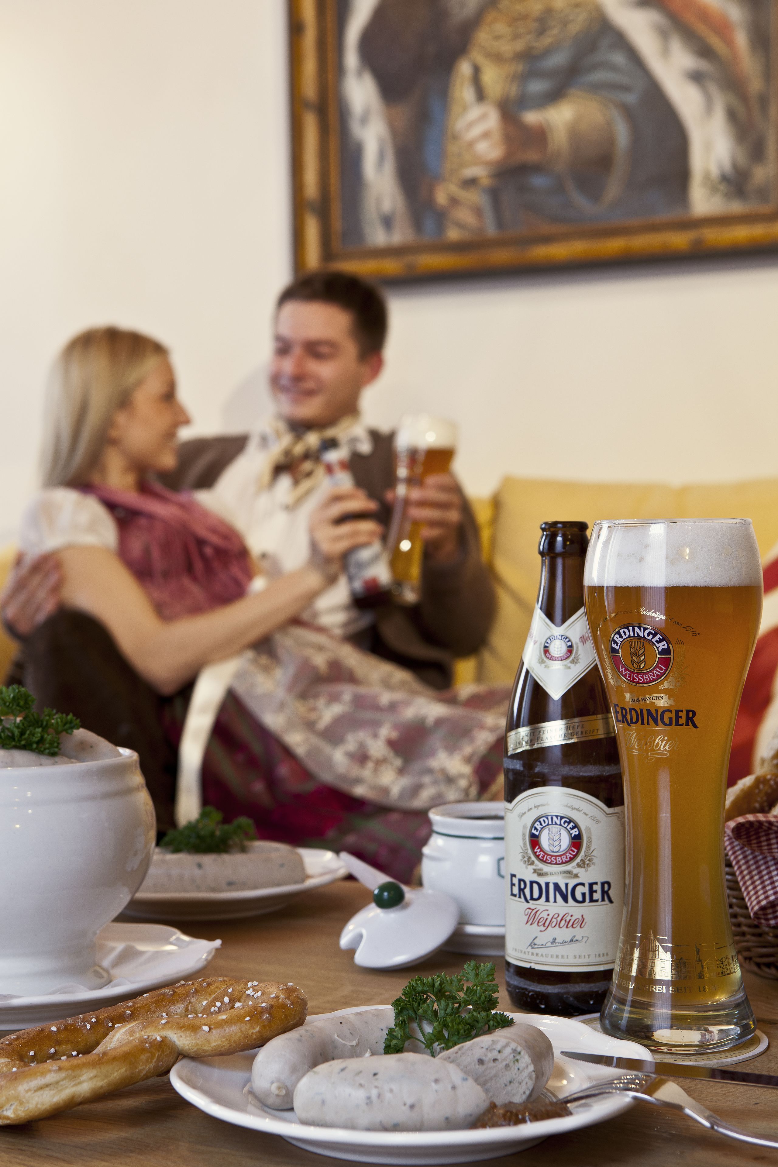 A dining table with a bottle of Erdinger Weissbier, a glass of beer, pretzels, and sausages.