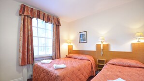 Ein Hotelzimmer mit zwei Betten, einem Fenster mit Vorhängen, Nachttischlampen und einem gerahmten Bild an der Wand.