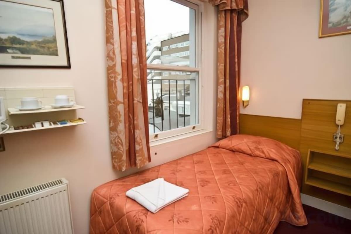 Ein Hotelzimmer mit Bett, einem Vorhangfenster, einem Heizkörper, einer Ablage mit Toilettenartikeln und einem an der Wand montierten Telefon.