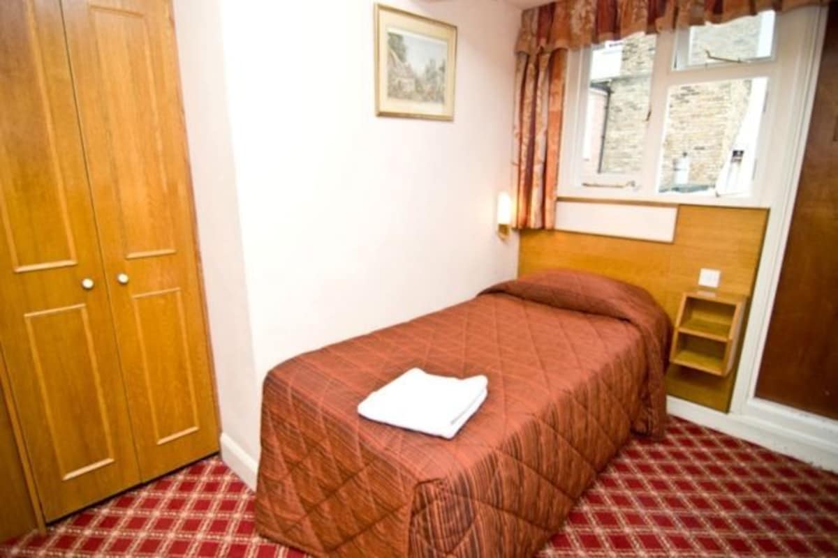 A bedroom with a bed, a wardrobe, a window with curtains, and a small shelf.