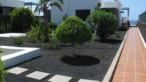 Een modern gebouw met een witte gevel, omgeven door een aangelegde tuin met diverse planten en een verhard pad.