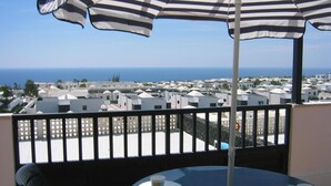 Een balkon met een gestreept parasol, een tafel met een kopje en schoteltje, en uitzicht op zee en gebouwen.