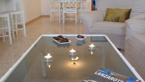 Een woonkamer met een glazen salontafel, twee kaarsen en een tijdschrift met de titel 'LANZAROTE'.