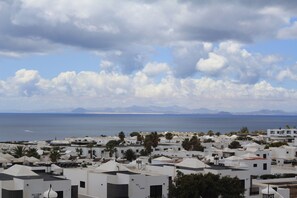 A coastal town with white buildings, palm trees, and a view of the sea and mountains in the distance.
