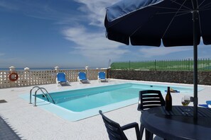 An outdoor swimming pool with lounge chairs and a table with a bottle and glass.