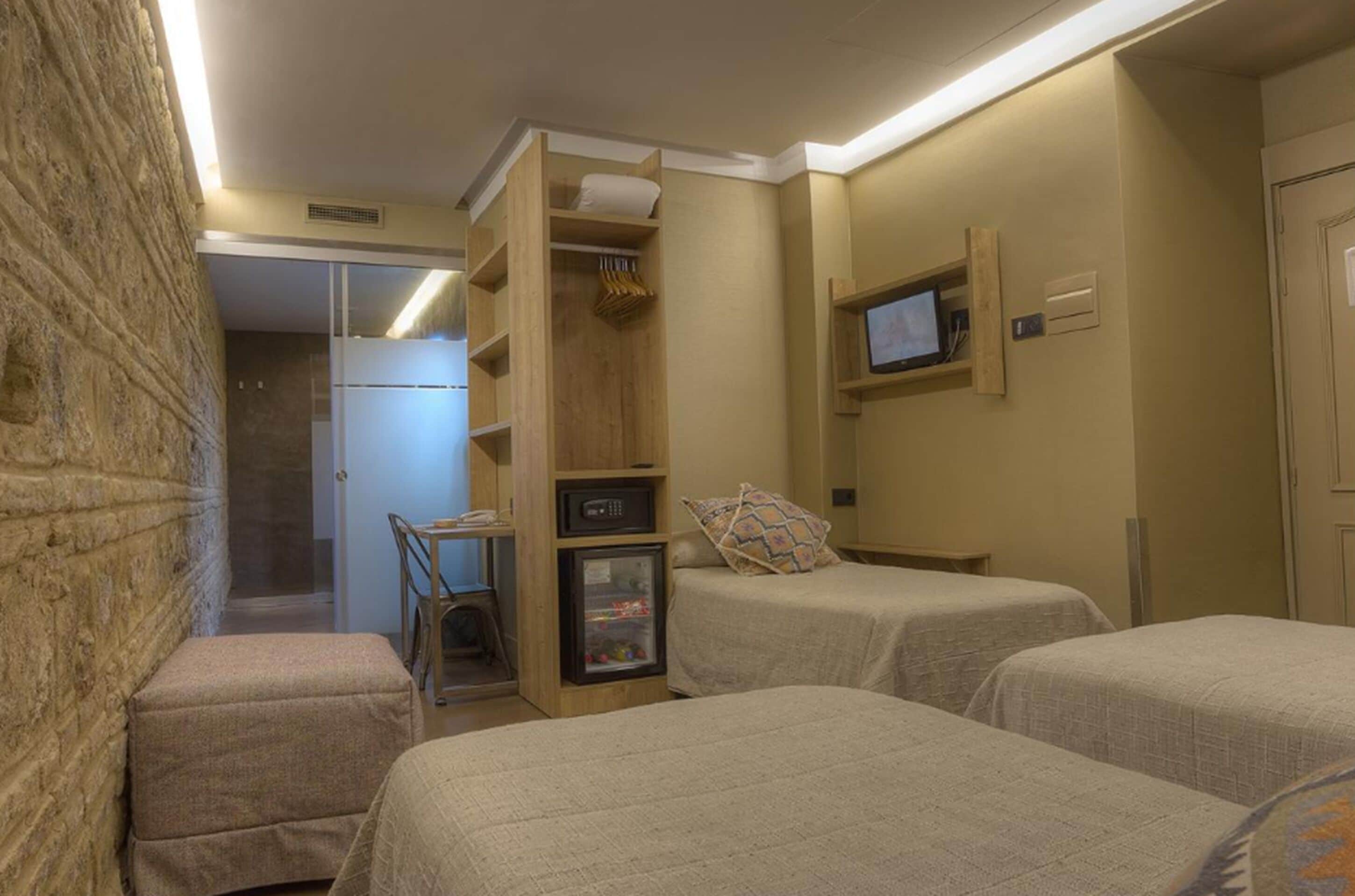 A hotel room with two beds, a small desk, a television, and a wardrobe.