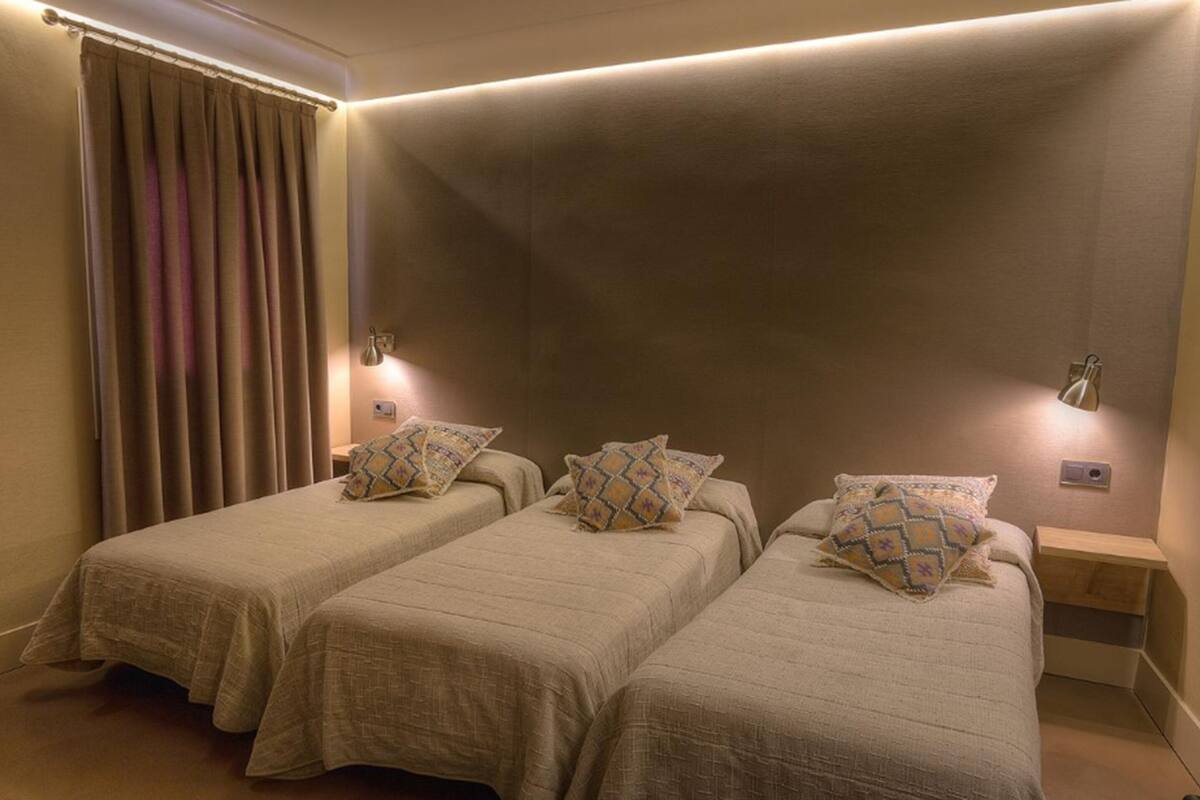 Ein Zimmer mit zwei Einzelbetten, jeweils mit einem gemusterten Kissen, einem Nachttisch und einer Wandlampe.