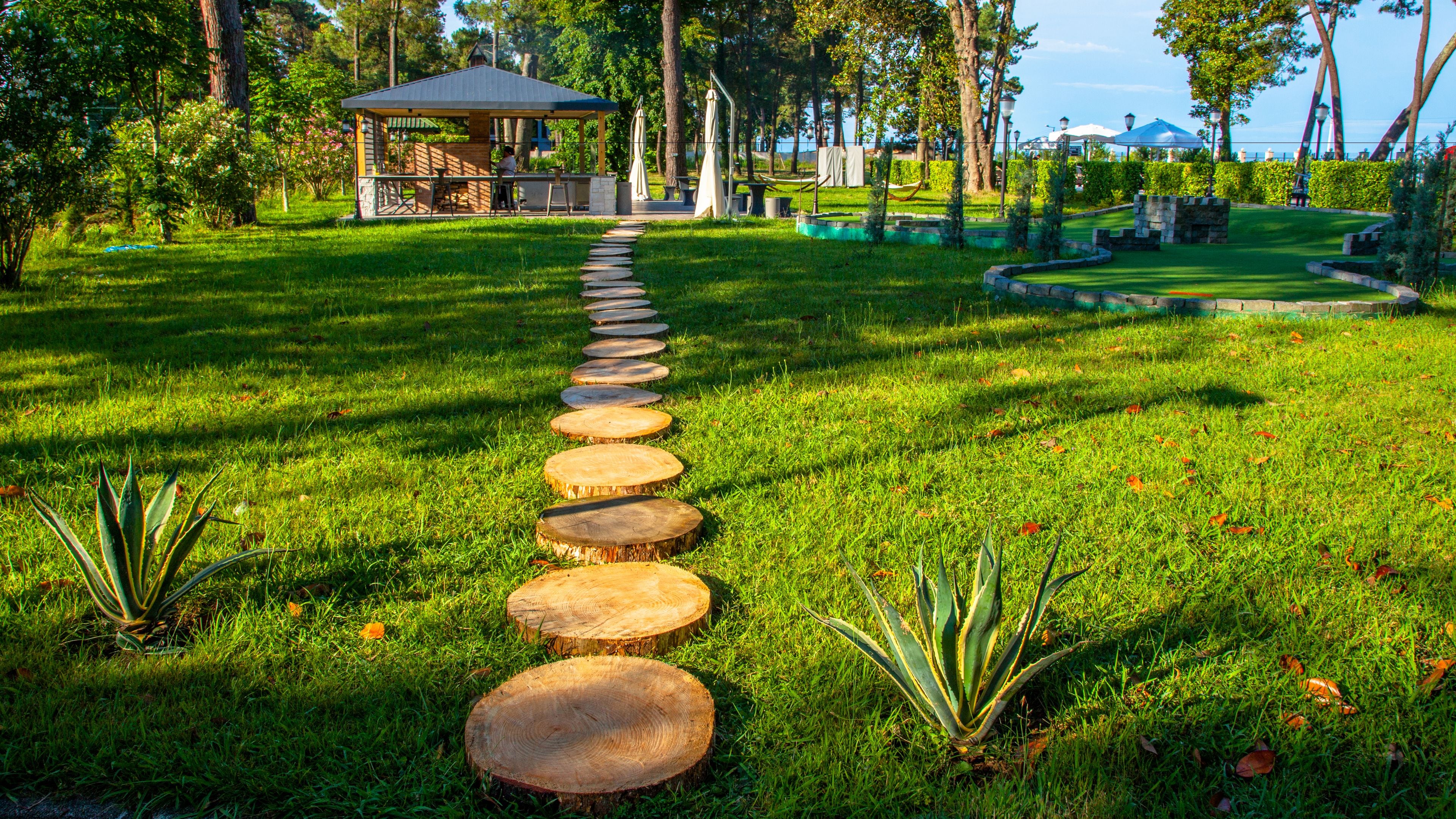 A pathway of wooden steps leading through a well-maintained garden with a gazebo and a small building in the background.