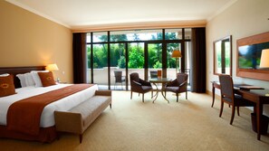 A hotel room with a large bed, a desk, two chairs, and a view of greenery through the windows. - Georgia Palace Hotel & SPA (Kobuleti)