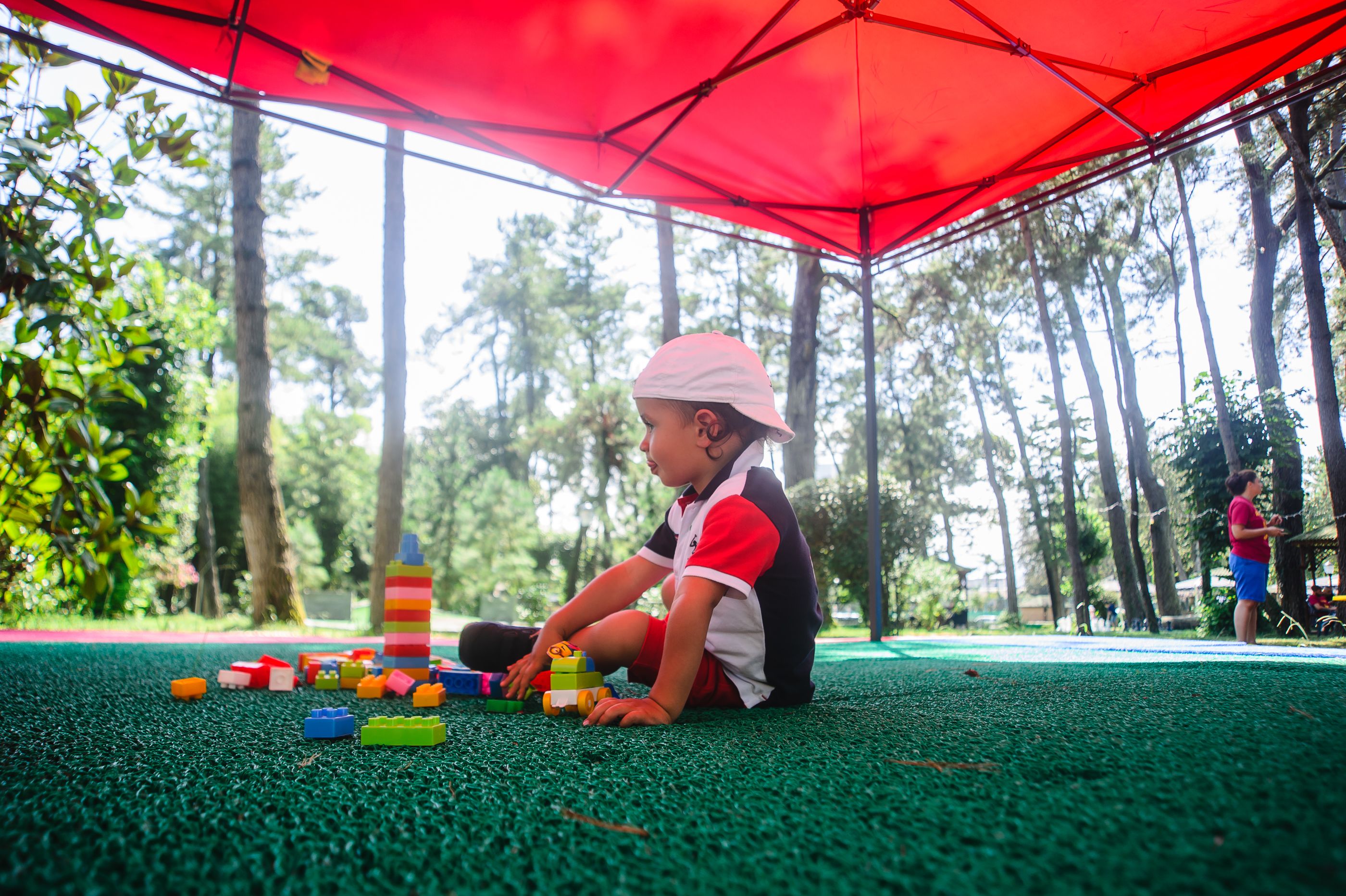 A child playing with colorful building blocks under a red umbrella in a park.