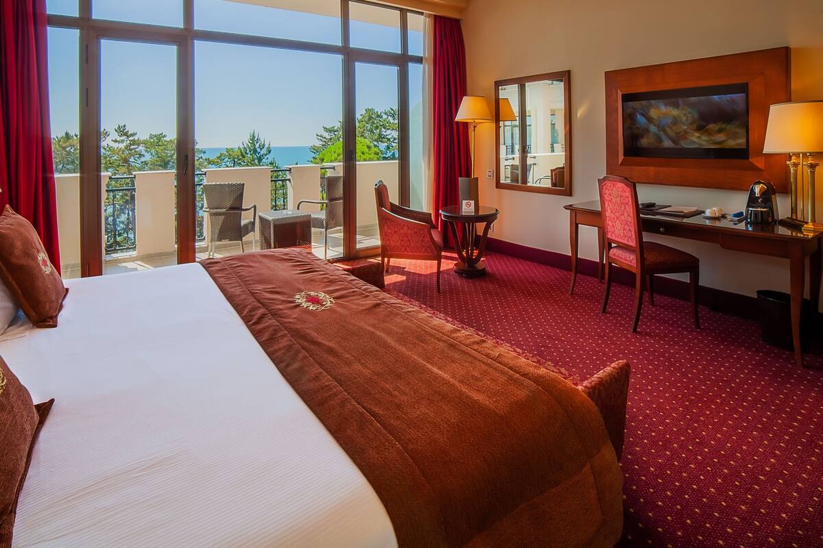 A hotel room with a large bed, a desk, a chair, and a balcony with a view.