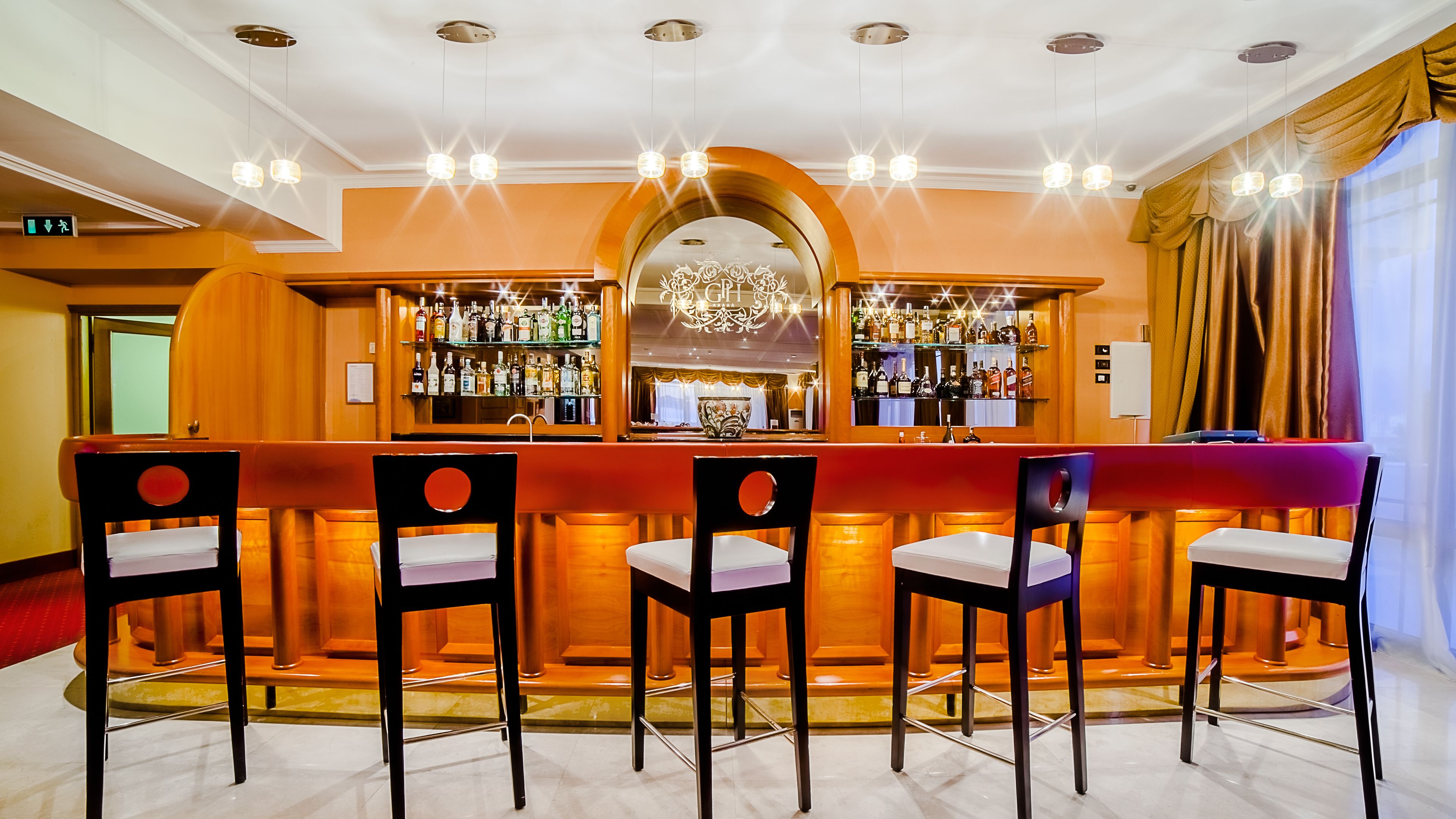 A bar area with a counter, multiple chairs, and a mirrored wall reflecting the bar.