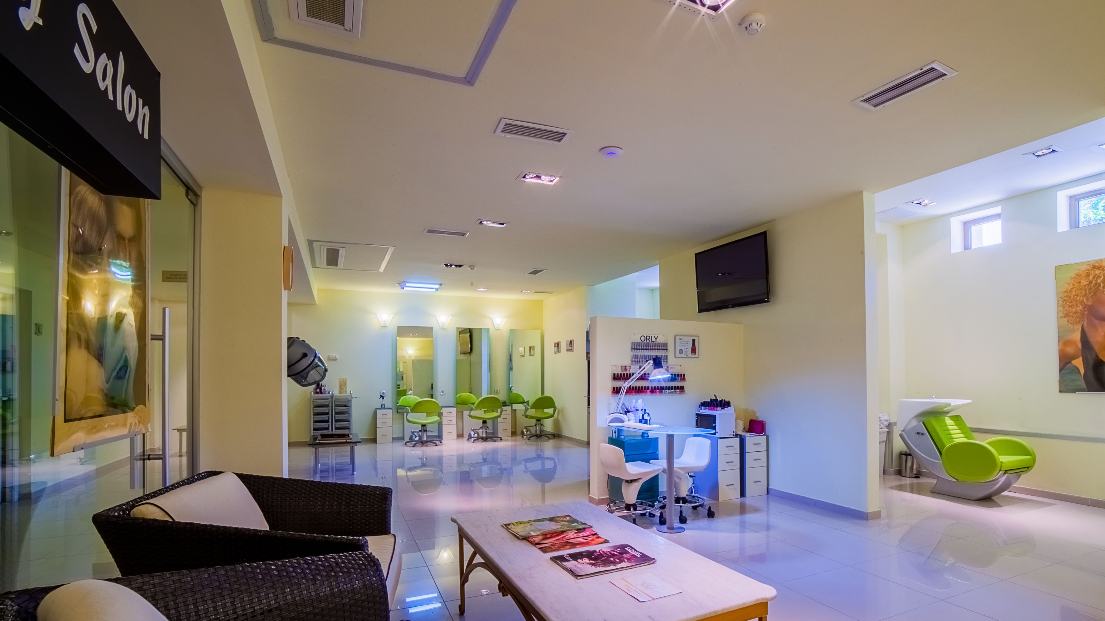 A modern salon interior with a reception desk, green chairs, and a large mirror.