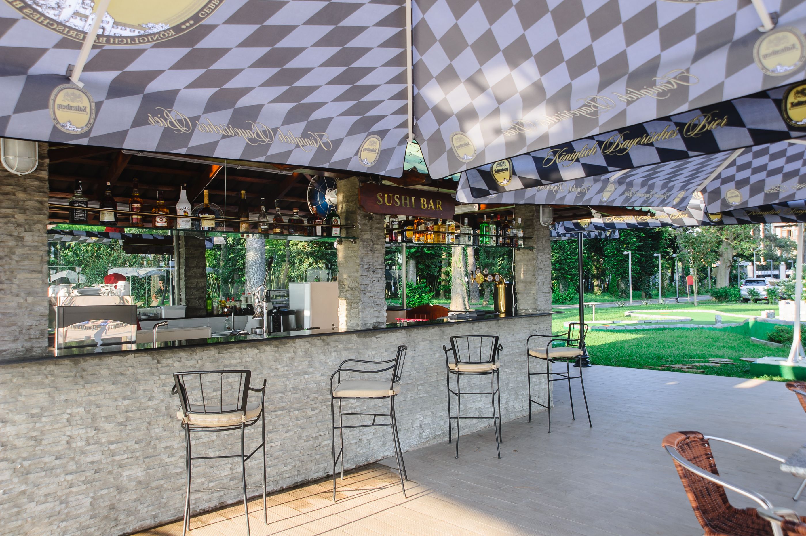A sushi bar with a checkered awning, outdoor seating with metal chairs, and a view of a landscaped garden.