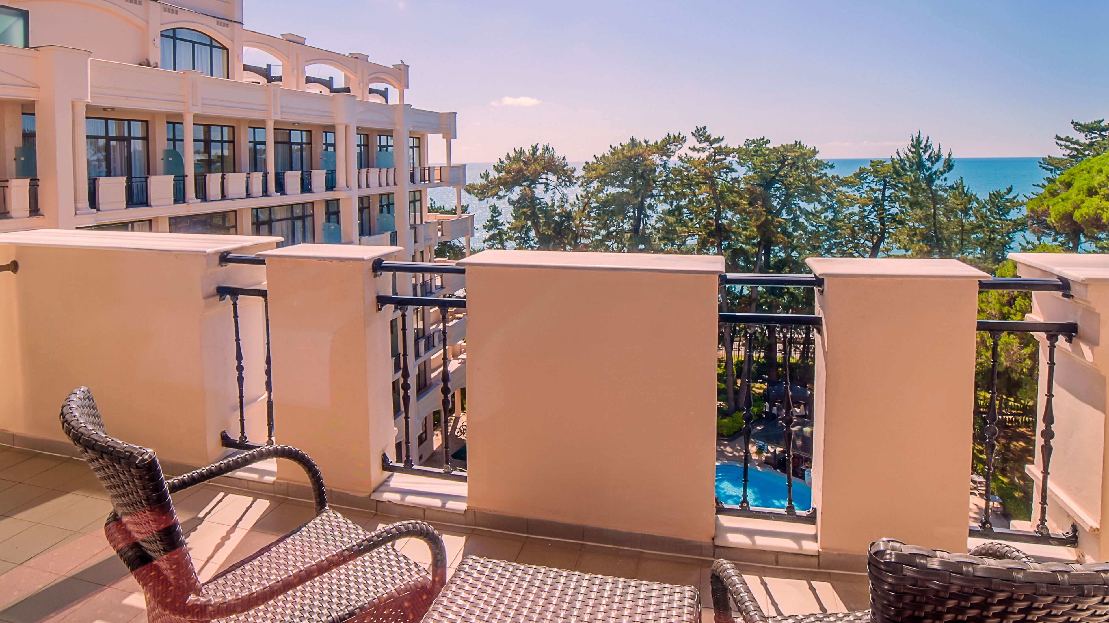 Un balcón con sillones de mimbre, vista a una piscina y un edificio con amplios ventanales.