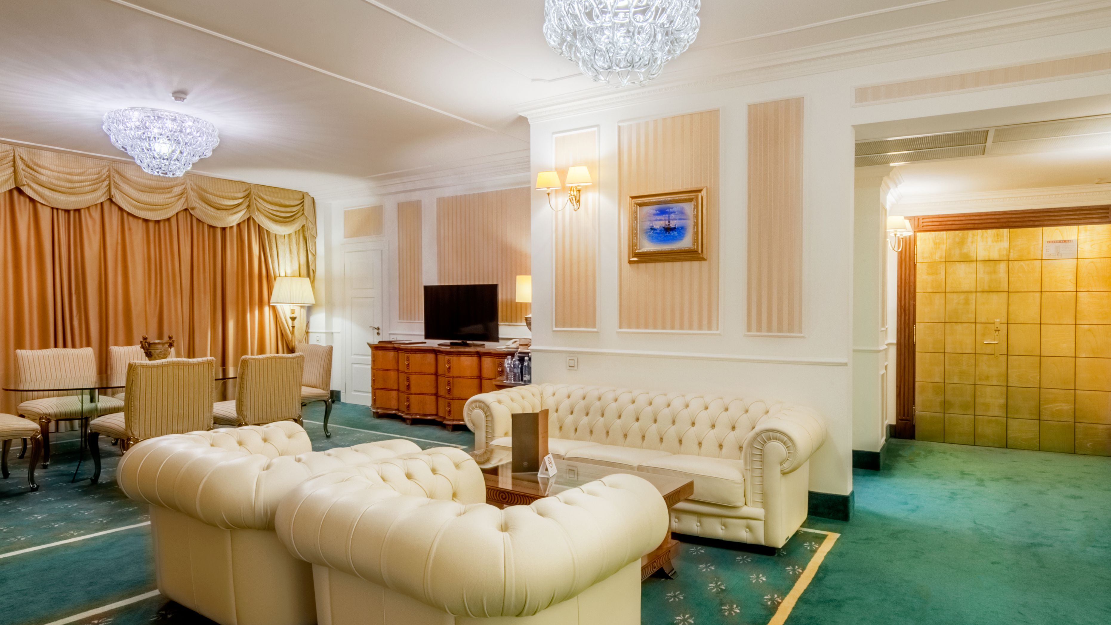 A spacious living room with a large sofa, a television, and a dining area with striped chairs.