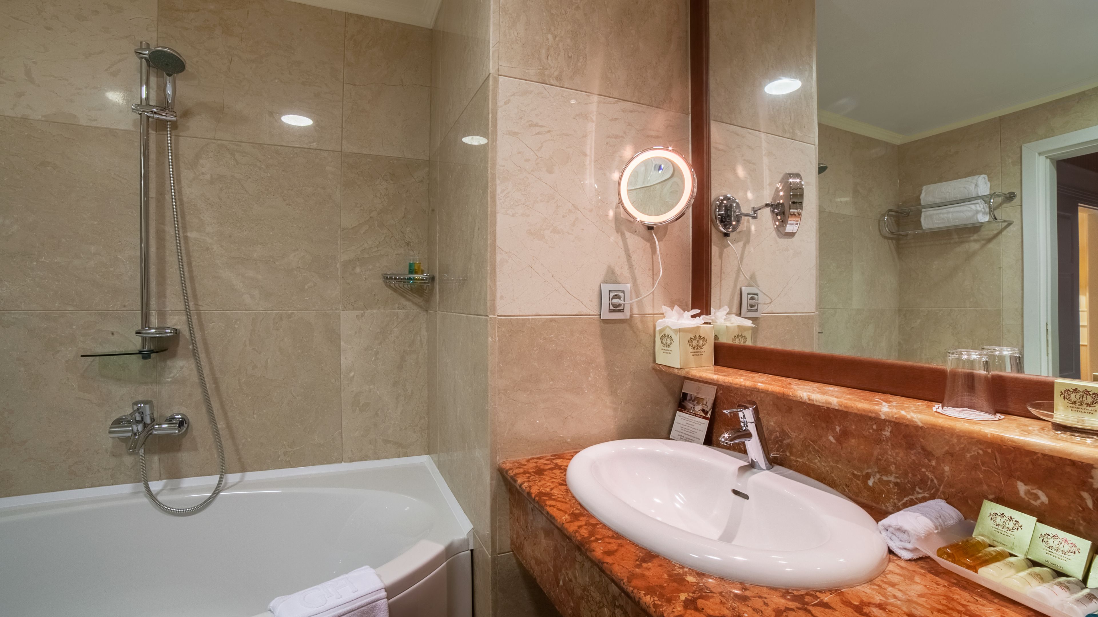 A bathroom with a bathtub, a shower, a sink, a vanity with a mirror, and toiletries.