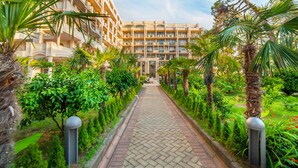 Un chemin bordé de palmiers et de verdure mène à un immeuble à plusieurs étages doté de balcons.