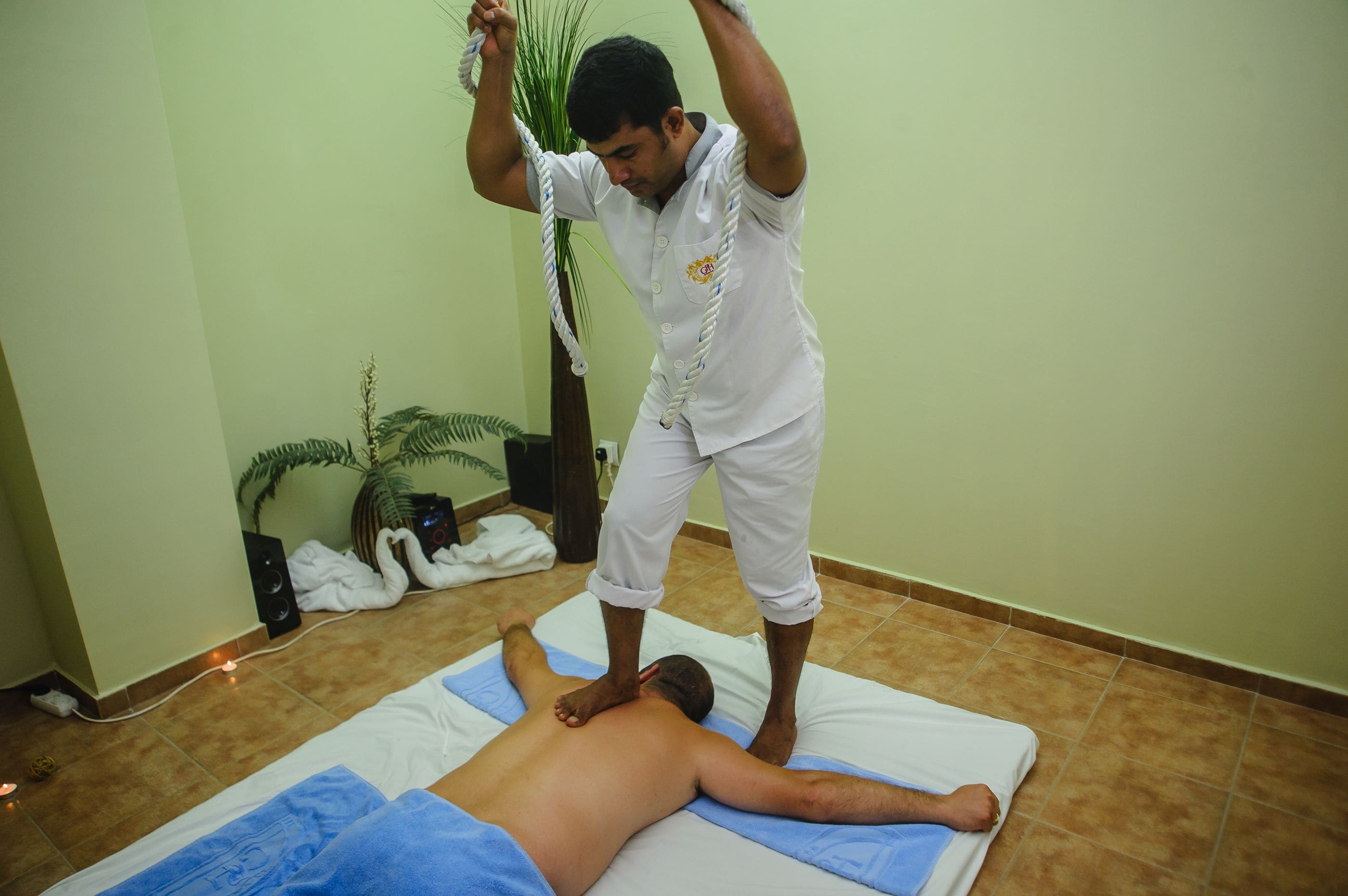 Une séance de massage dans une pièce dont le sol est carrelé, qui contient une table de massage et une plante en pot.
