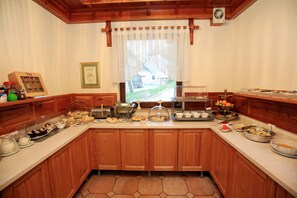 A kitchen with wooden cabinets, a breakfast bar, and various food items displayed on the counter. - Hotel Gasperin (Bohinj)