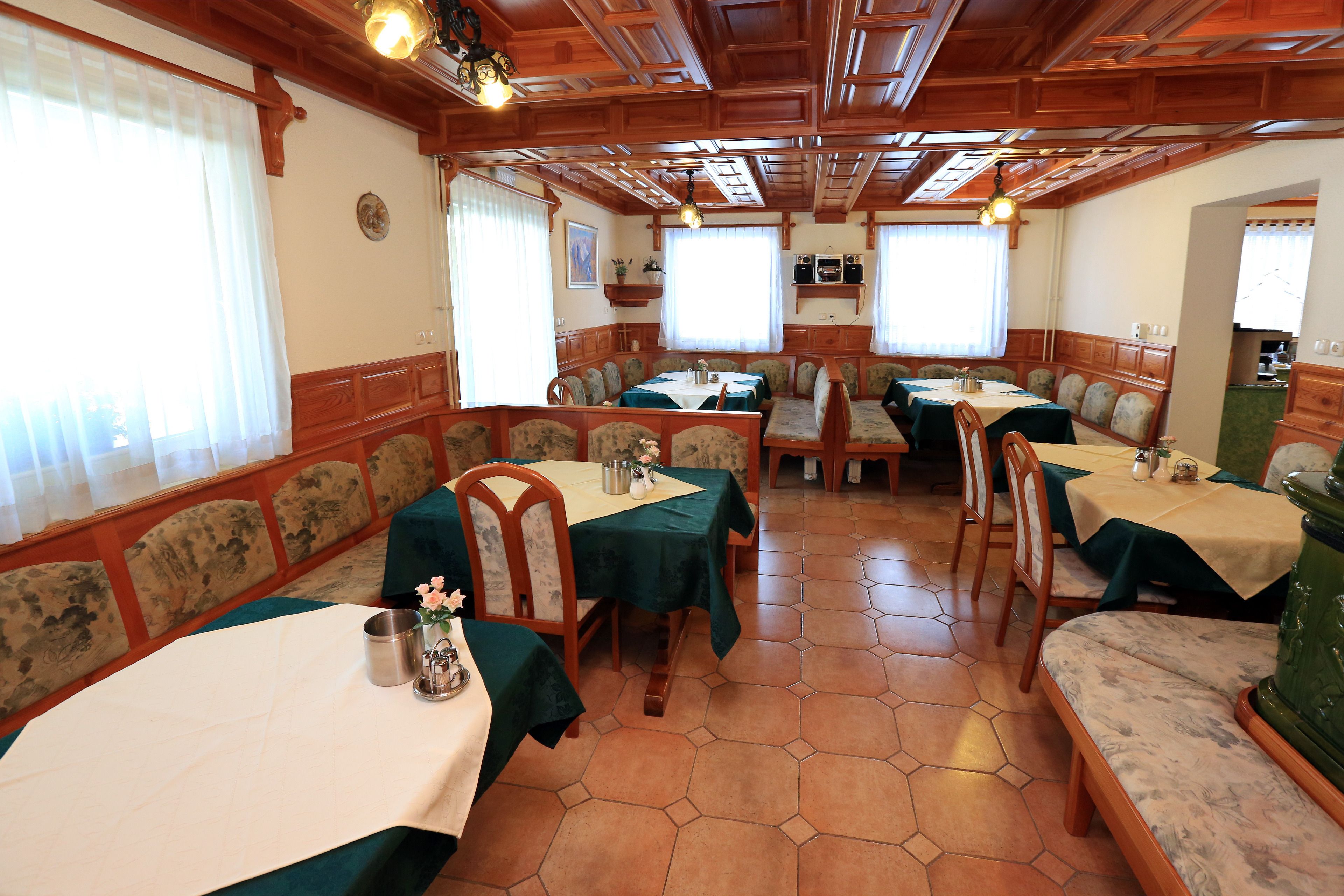 Zona de dinar amb sòcols hexagonals, revestiment de fusta a les parets i taules cobertes amb mantells verds i cadires.