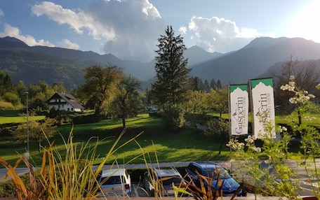 A rural landscape with a mountain backdrop, a white building, and parked cars.