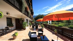 Eine Terrassengruppe mit Korbmöbeln, Blumentöpfen und orangefarbenen Sonnenschirmen.