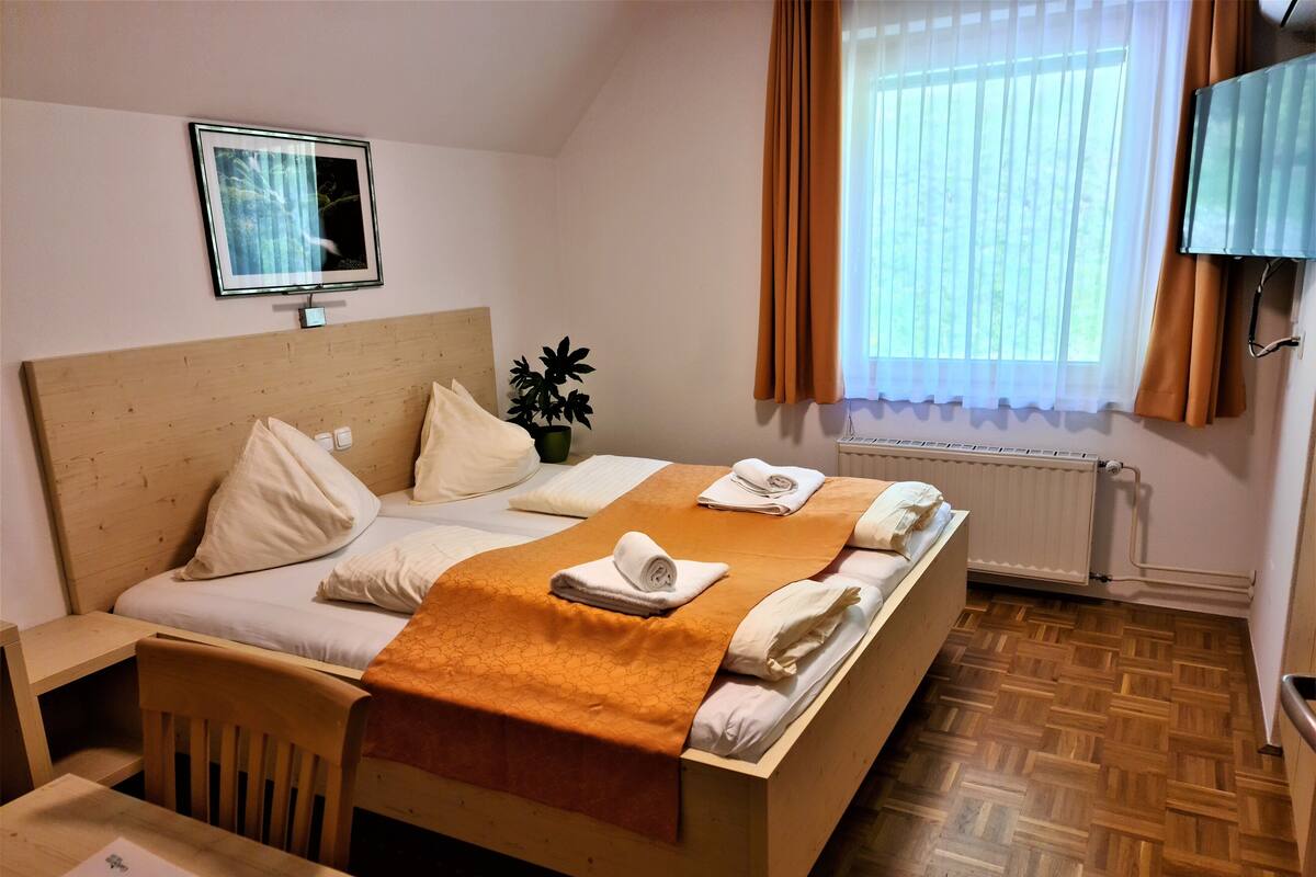 A hotel room with a bed, a desk, a chair, a TV, and a window with curtains.